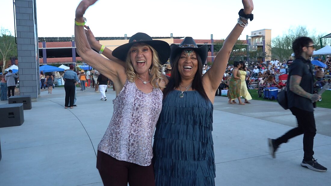 Two guests in hats cheering with the packed lawn behind them