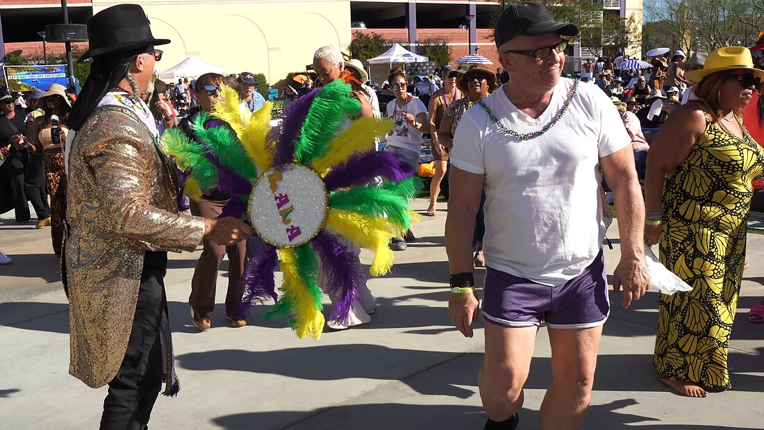 A second line dancer in a sequined jacket with a feathered fan dancing with a guest
