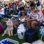 Two women seated with their poodle among festival tents at Soul Springs Festival